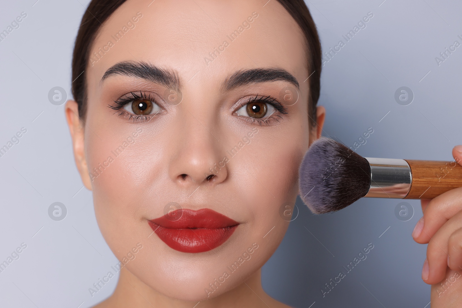 Image of Beautiful woman applying makeup with brush on light grey background, closeup