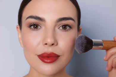 Image of Beautiful woman applying makeup with brush on light grey background, closeup