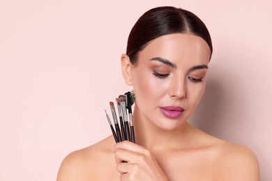Image of Beautiful woman with makeup brushes on light pink background