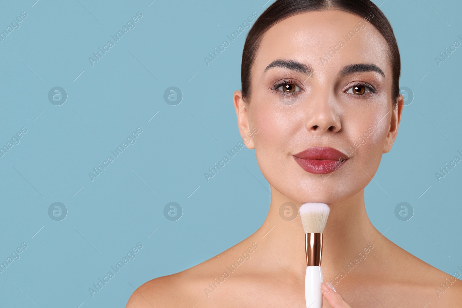Image of Beautiful woman with makeup brush on light blue background