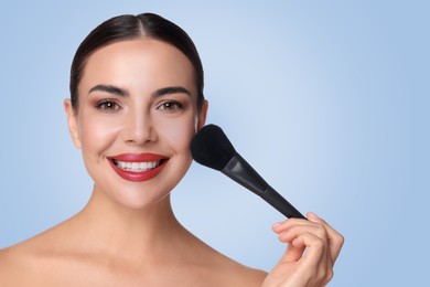 Image of Beautiful woman applying makeup with brush on light blue background