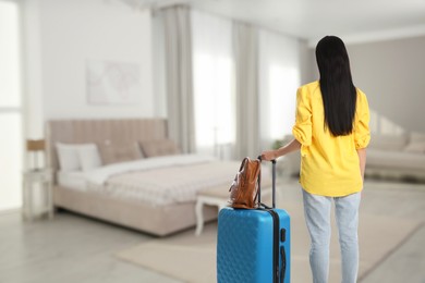 Image of Woman with suitcase and bag in hotel room, back view