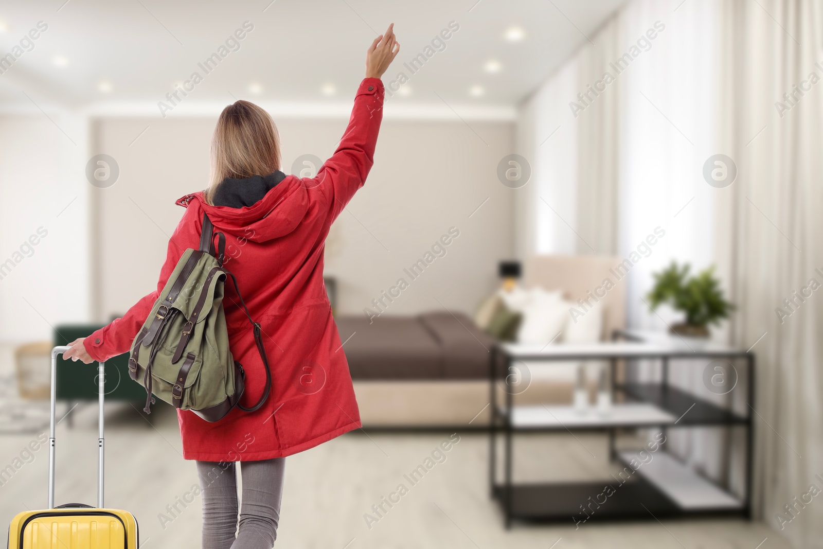 Image of Woman with suitcase and backpack in hotel room, back view