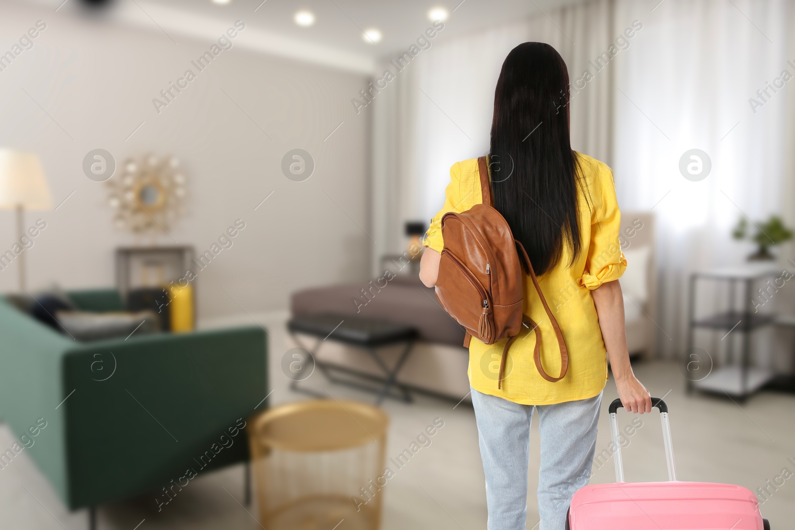 Image of Woman with suitcase and backpack in hotel room, back view