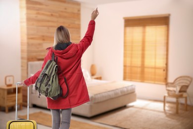 Image of Woman with suitcase and backpack in hotel room, back view