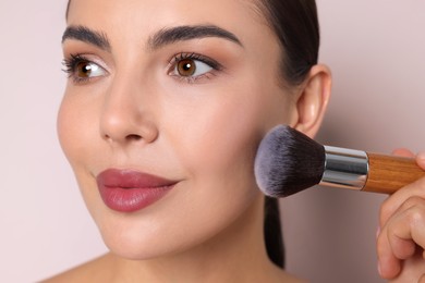 Image of Beautiful woman applying makeup with brush on beige background, closeup