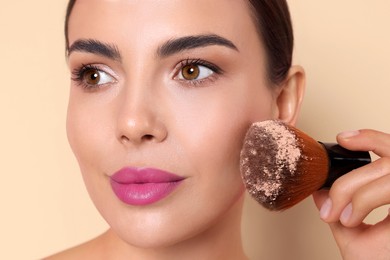 Image of Beautiful woman applying makeup with brush on beige background, closeup