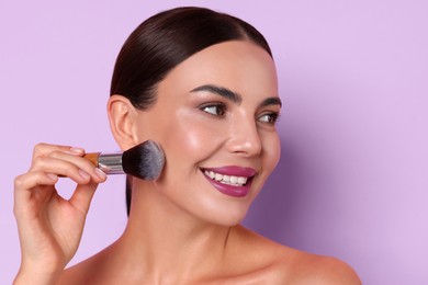 Image of Beautiful woman applying makeup with brush on light violet background