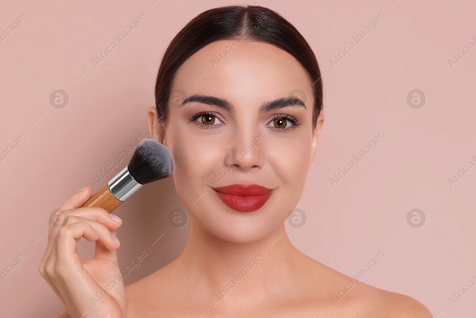 Image of Beautiful woman applying makeup with brush on pink beige background