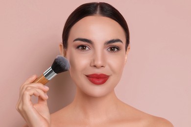 Image of Beautiful woman applying makeup with brush on pink beige background