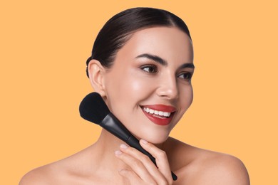 Image of Beautiful woman with makeup brush on pale orange background
