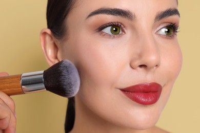 Image of Beautiful woman applying makeup with brush on dark beige background, closeup