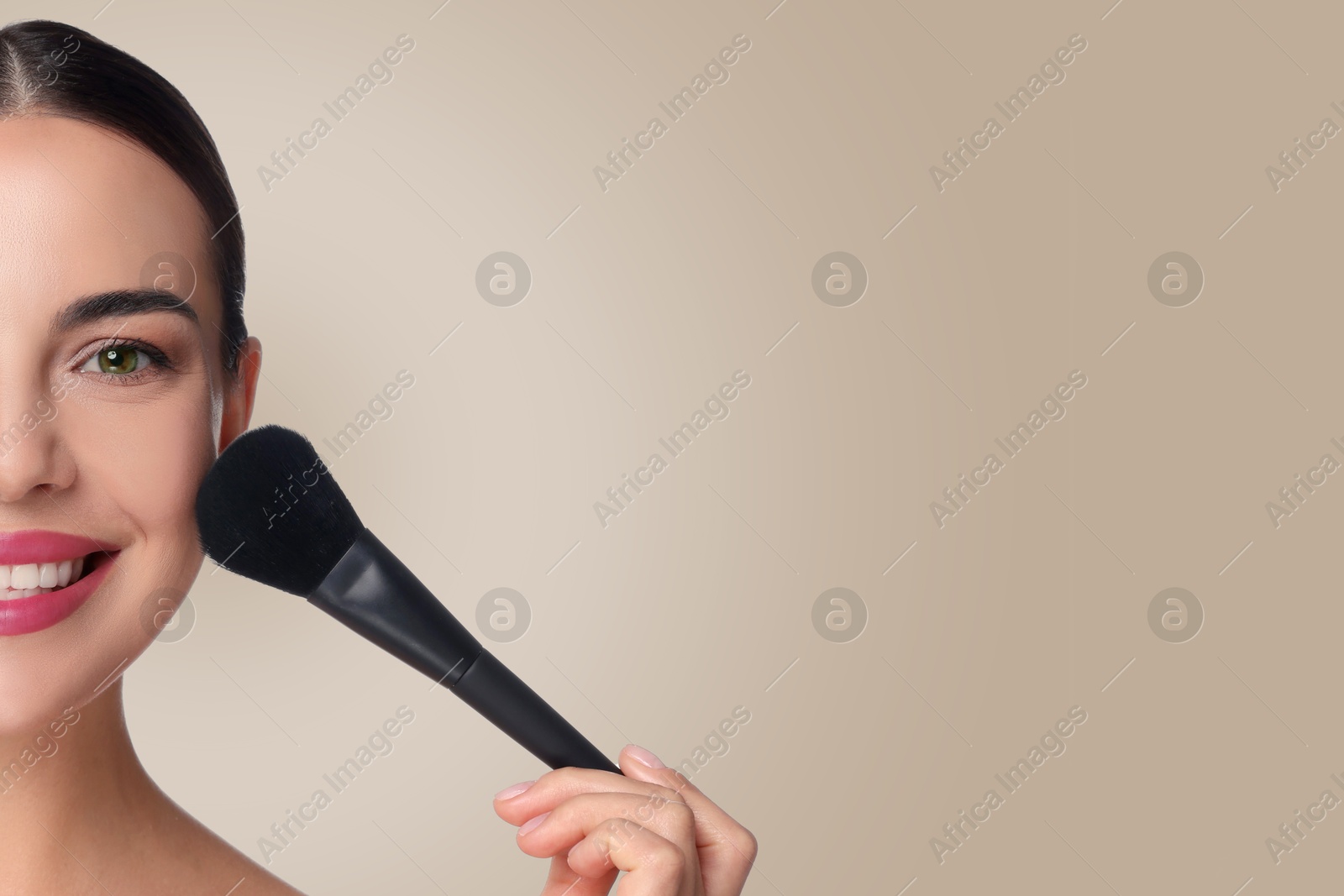 Image of Beautiful woman applying makeup with brush on grey beige background. Space for text