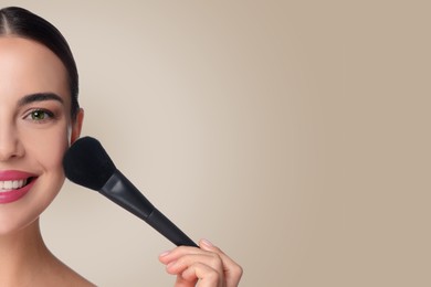 Image of Beautiful woman applying makeup with brush on grey beige background. Space for text