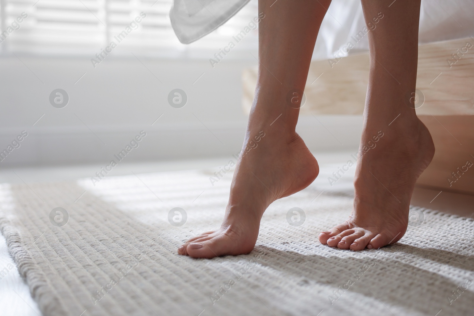 Photo of Woman walking barefoot on soft beige carpet near bed at home, closeup. Space for text