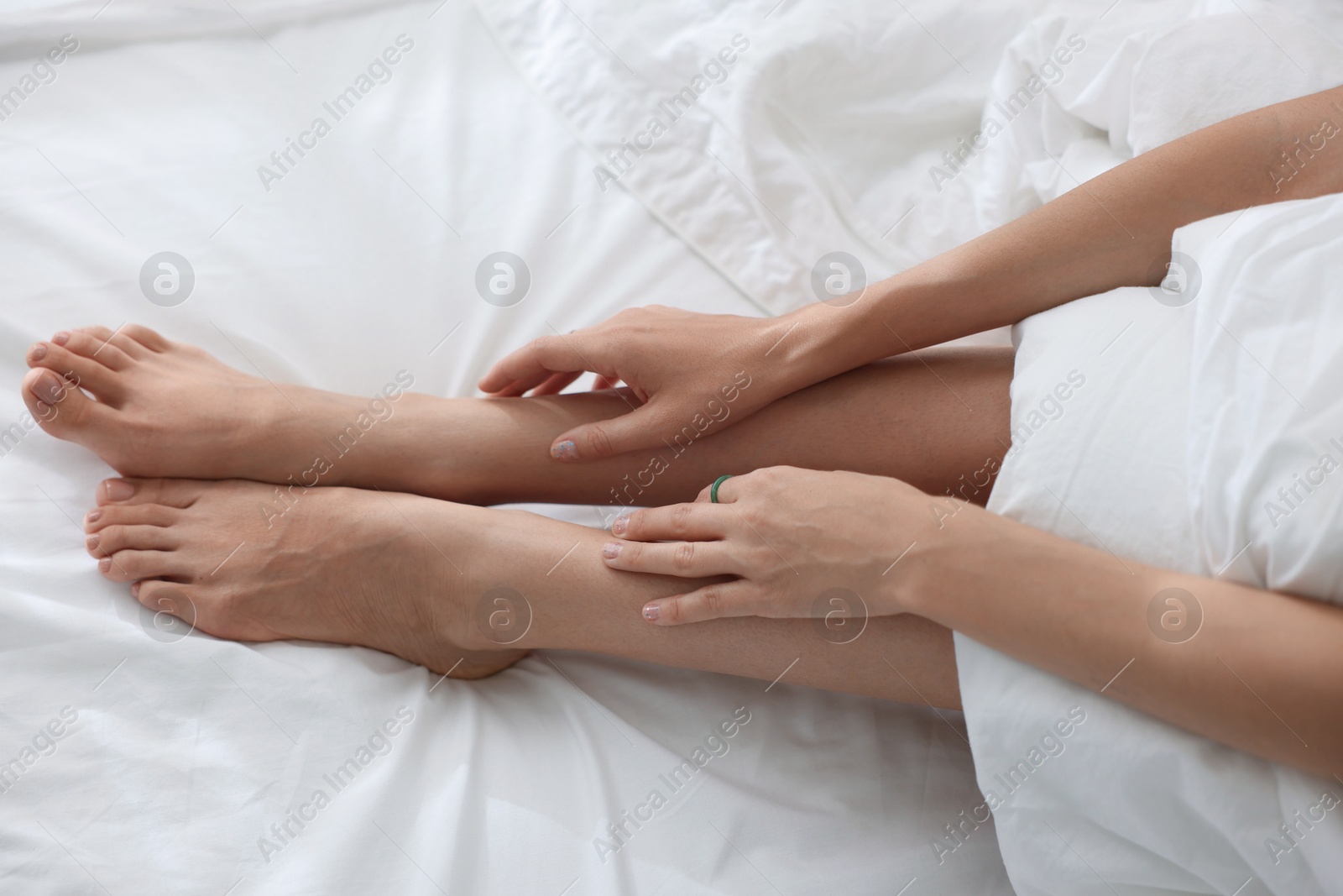 Photo of Woman barefoot on bed with white linens, above view
