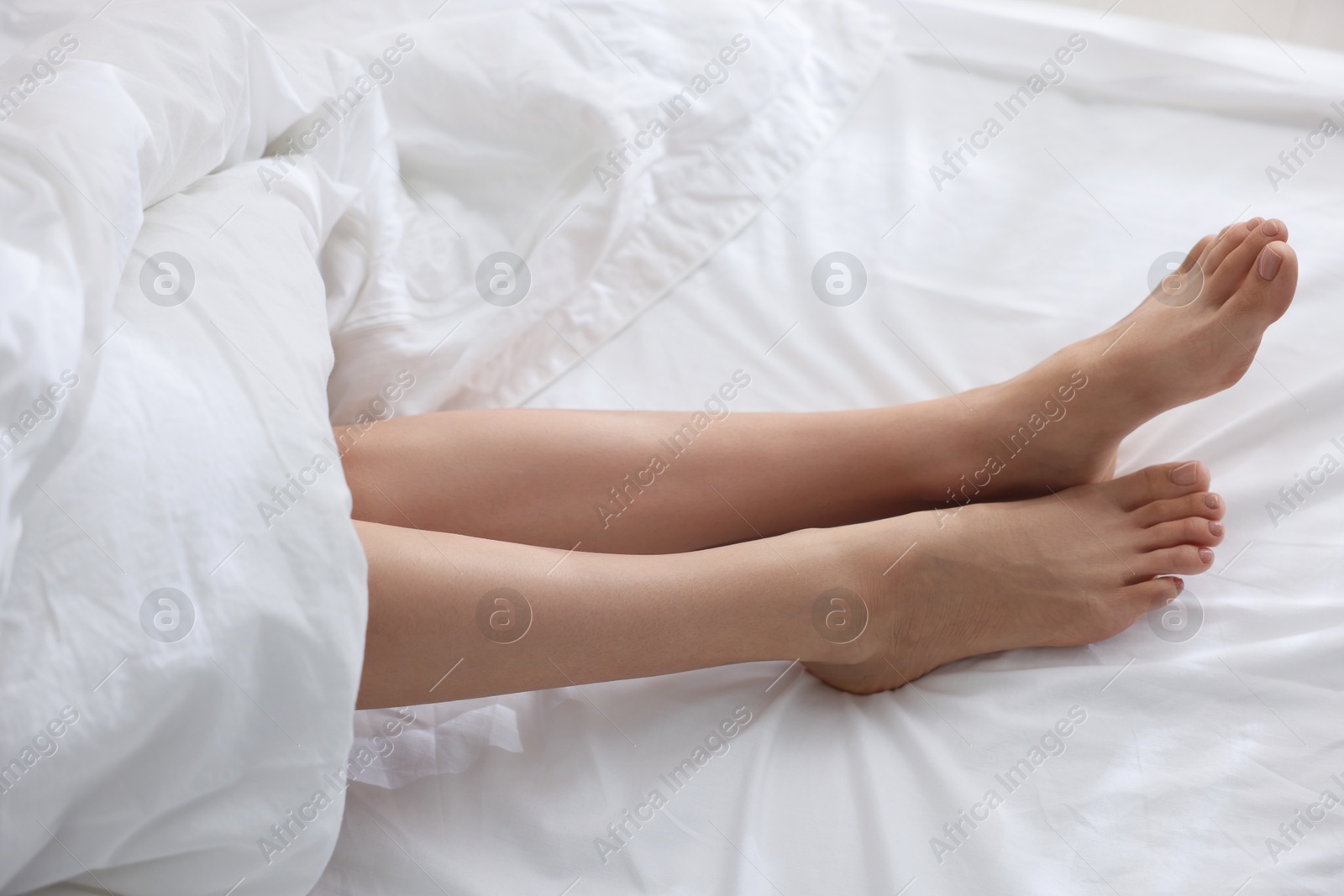 Photo of Woman barefoot on bed with white linens, closeup