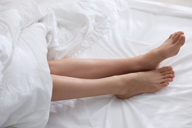 Photo of Woman barefoot on bed with white linens, closeup