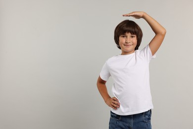 Photo of Little boy measuring his height on grey background, space for text