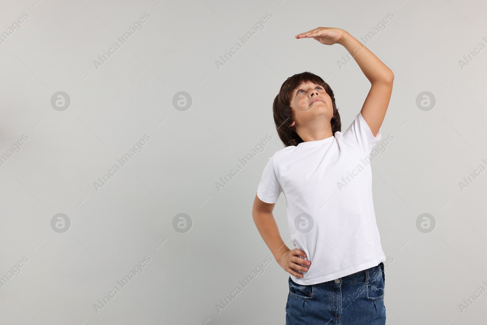 Photo of Little boy measuring his height on grey background, space for text