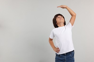 Photo of Little boy measuring his height on grey background, space for text