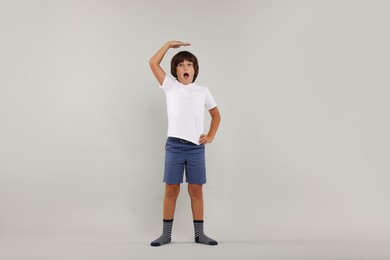 Photo of Emotional boy measuring his height on grey background