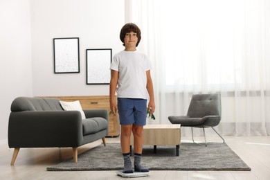 Photo of Cute boy standing on scales at home