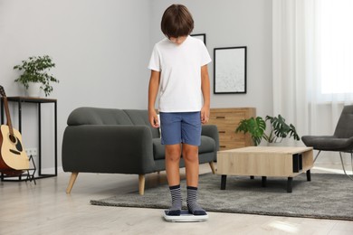 Photo of Cute boy standing on scales at home