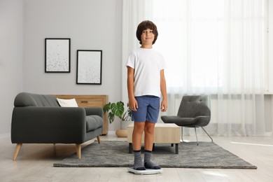 Photo of Cute boy standing on scales at home