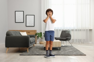 Photo of Emotional boy standing on scales at home