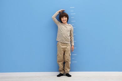 Photo of Cute boy measuring his height near blue wall indoors