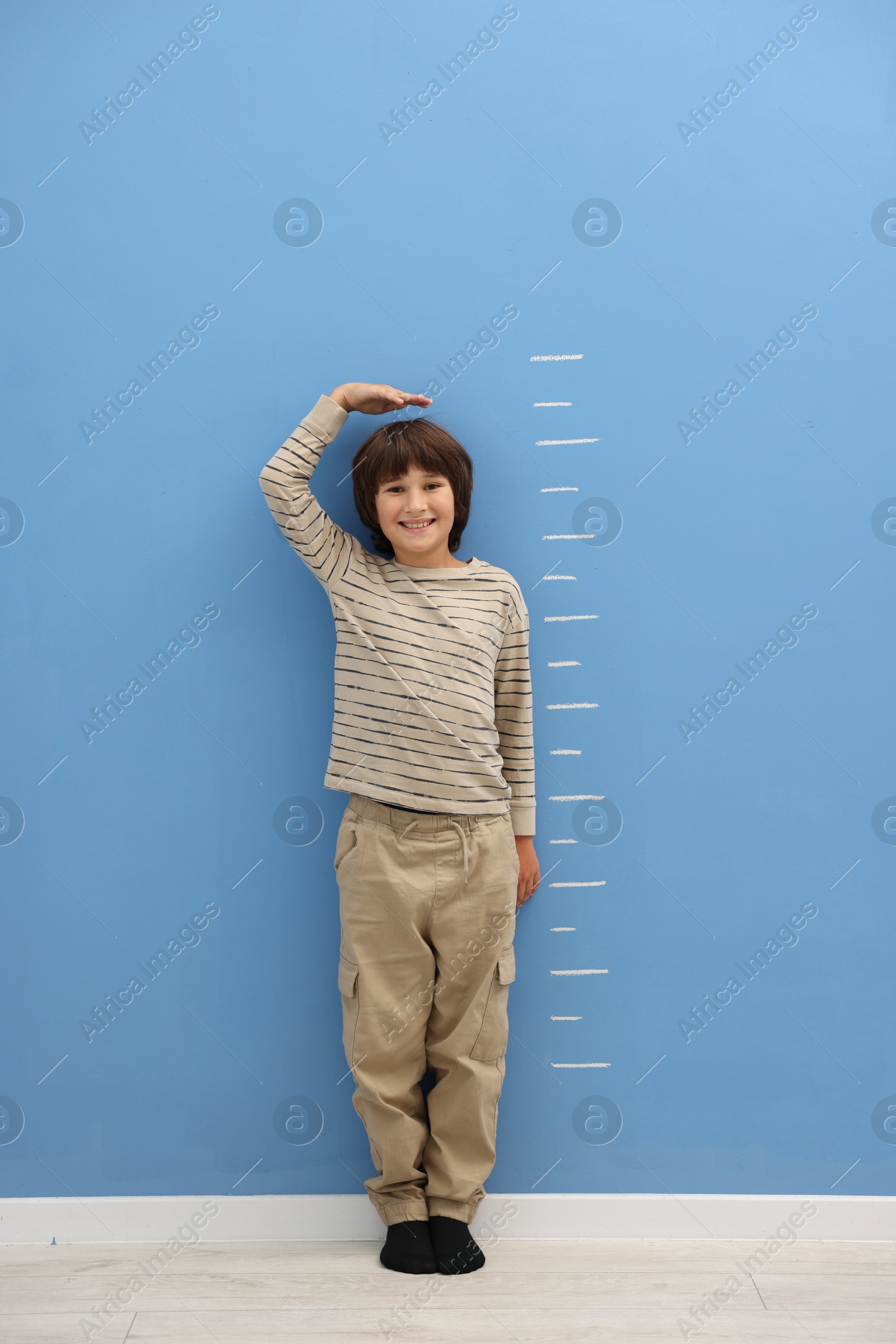 Photo of Cute boy measuring his height near blue wall indoors