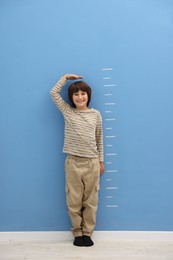 Photo of Cute boy measuring his height near blue wall indoors