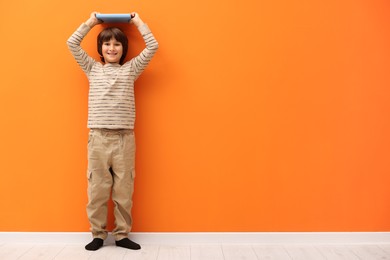 Photo of Cute boy measuring his height near orange wall indoors. Space for text