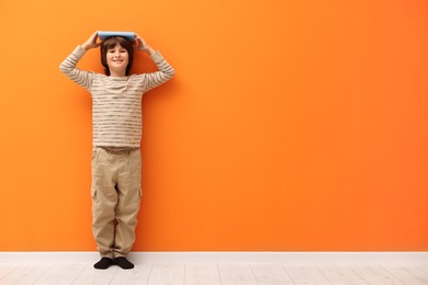 Photo of Cute boy measuring his height near orange wall indoors. Space for text