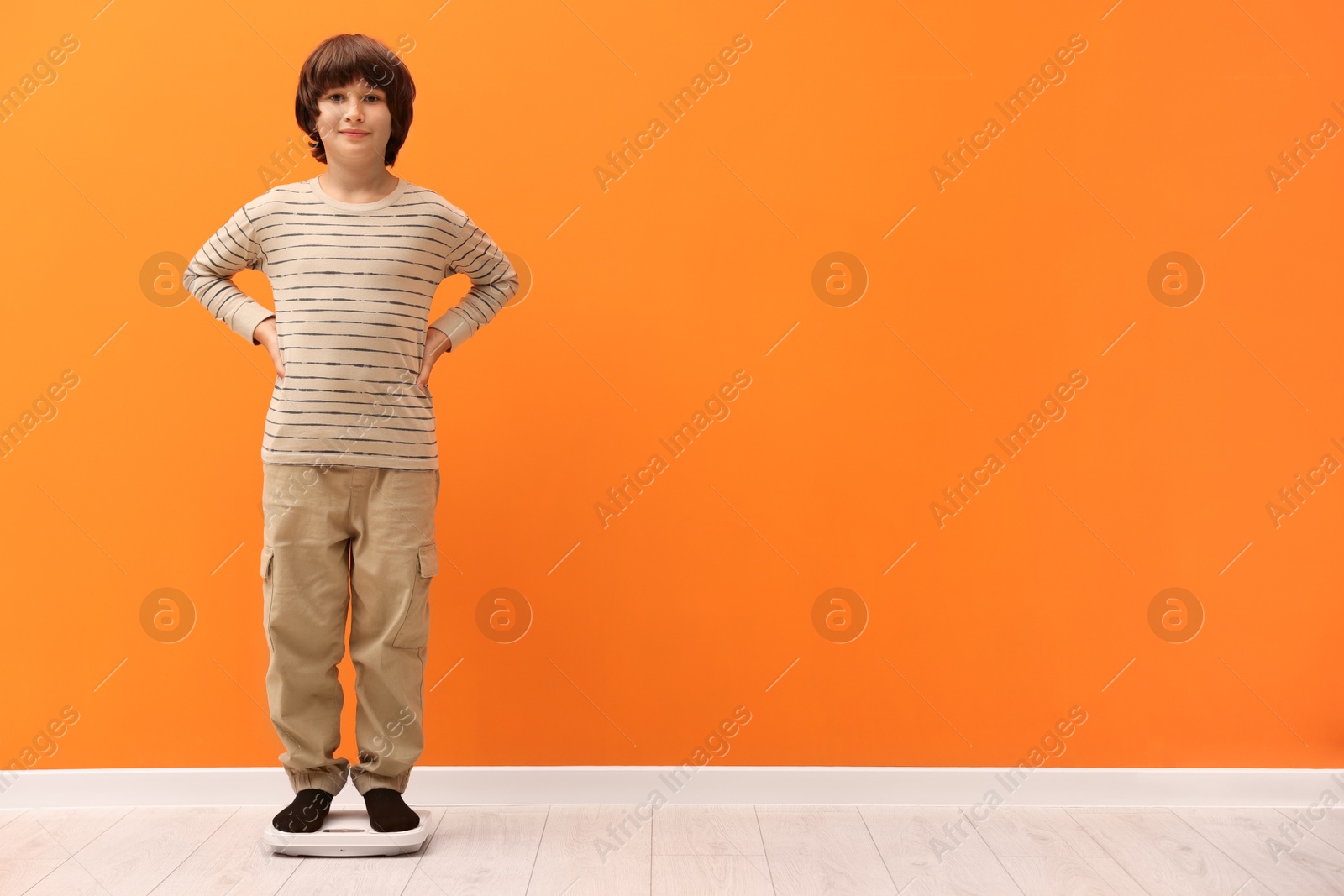 Photo of Little boy standing on scales near orange wall indoors. Space for text