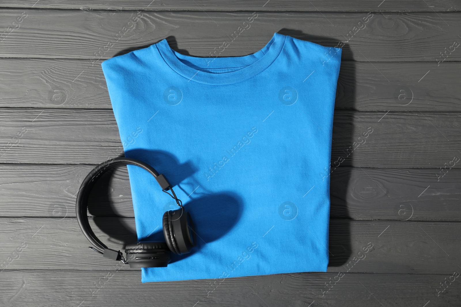 Photo of Light blue t-shirt and headphones on grey wooden table, top view. Mockup for design