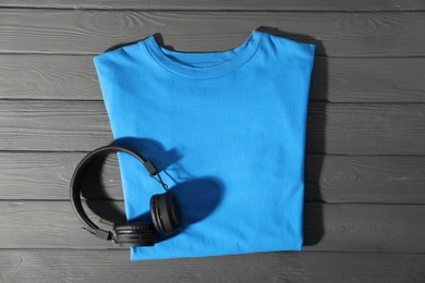 Photo of Light blue t-shirt and headphones on grey wooden table, top view. Mockup for design