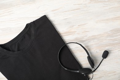 Photo of Black t-shirt and headset on wooden table, top view. Mockup for design