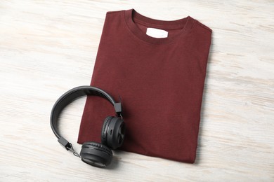 Photo of Brown t-shirt and headphones on wooden table, top view. Mockup for design