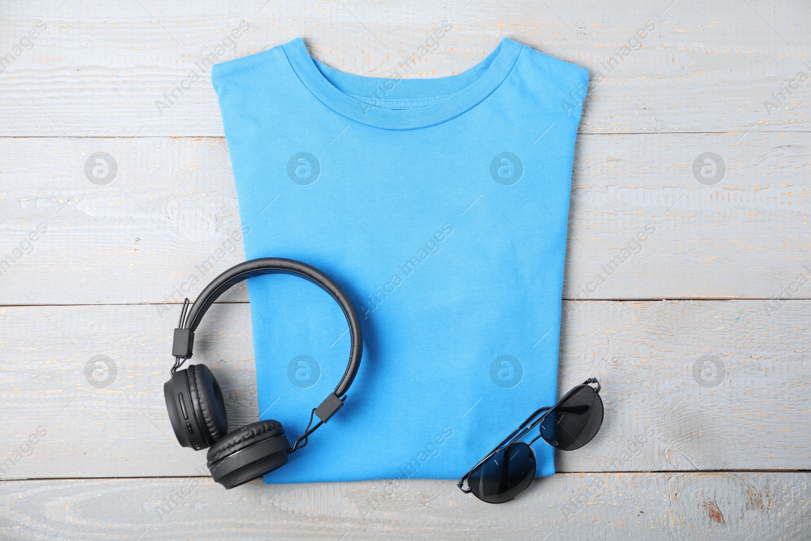 Photo of Light blue t-shirt, headphones and sunglasses on wooden table, flat lay. Mockup for design