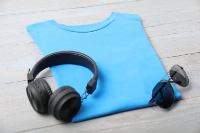Photo of Light blue t-shirt, headphones and sunglasses on wooden table, closeup. Mockup for design