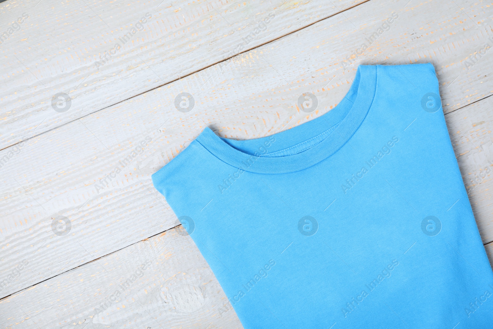 Photo of Light blue t-shirt on wooden table, top view. Mockup for design