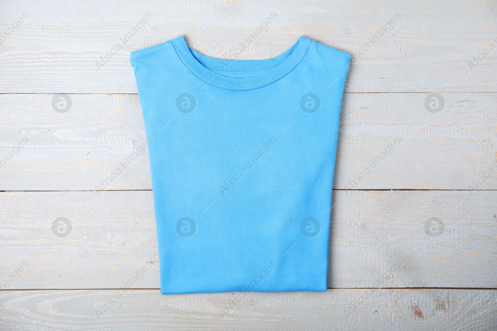 Photo of Light blue t-shirt on wooden table, top view. Mockup for design