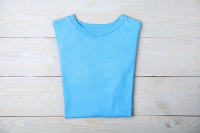 Photo of Light blue t-shirt on wooden table, top view. Mockup for design