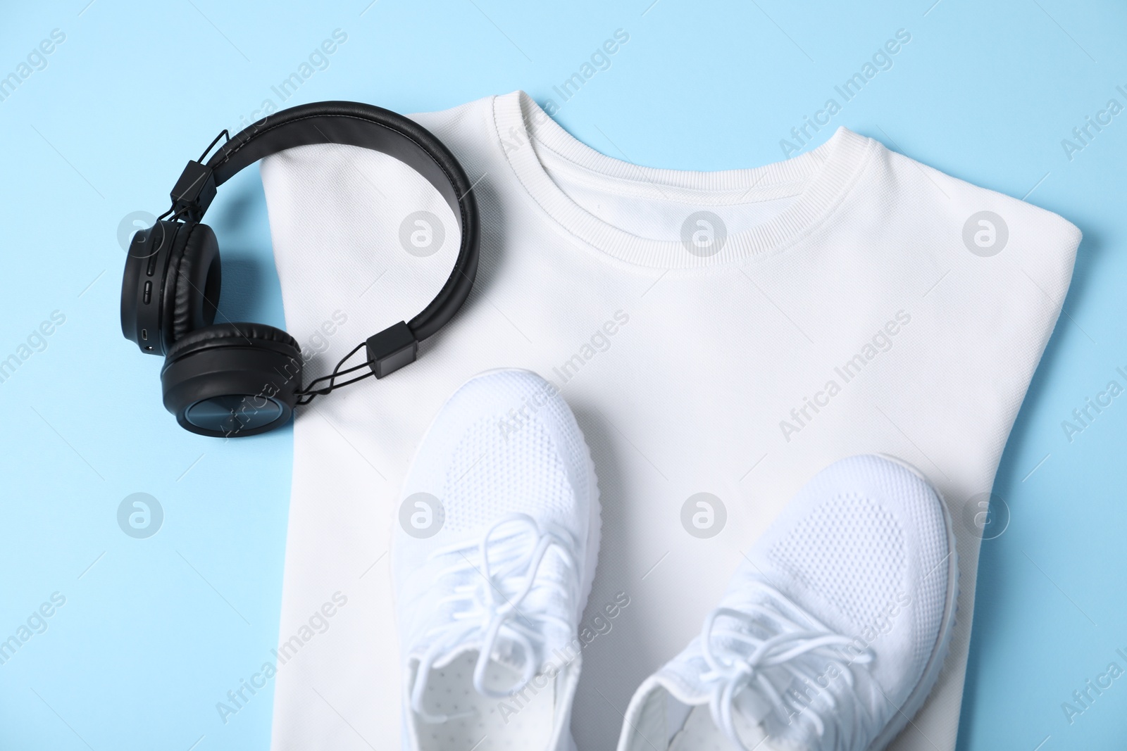 Photo of White t-shirt, sneakers and headphones on light blue background, top view. Mockup for design