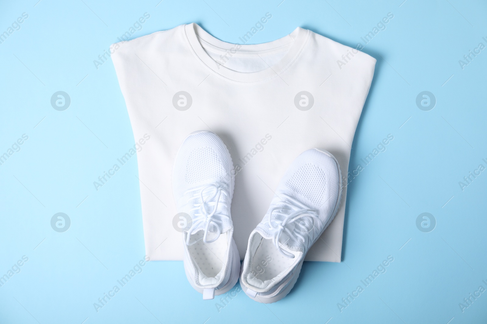 Photo of White t-shirt and sneakers on light blue background, top view. Mockup for design