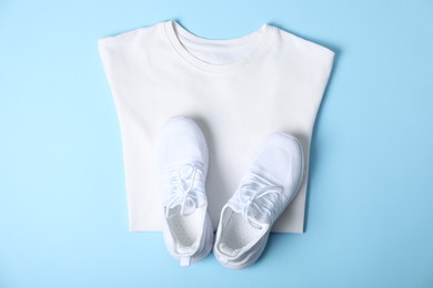 Photo of White t-shirt and sneakers on light blue background, top view. Mockup for design