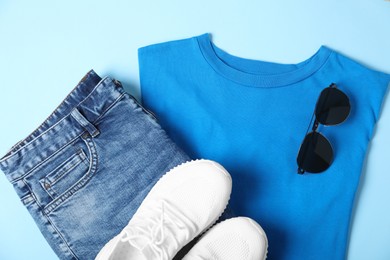 Photo of T-shirt, jeans, sunglasses and sneakers on light blue background, flat lay. Mockup for design