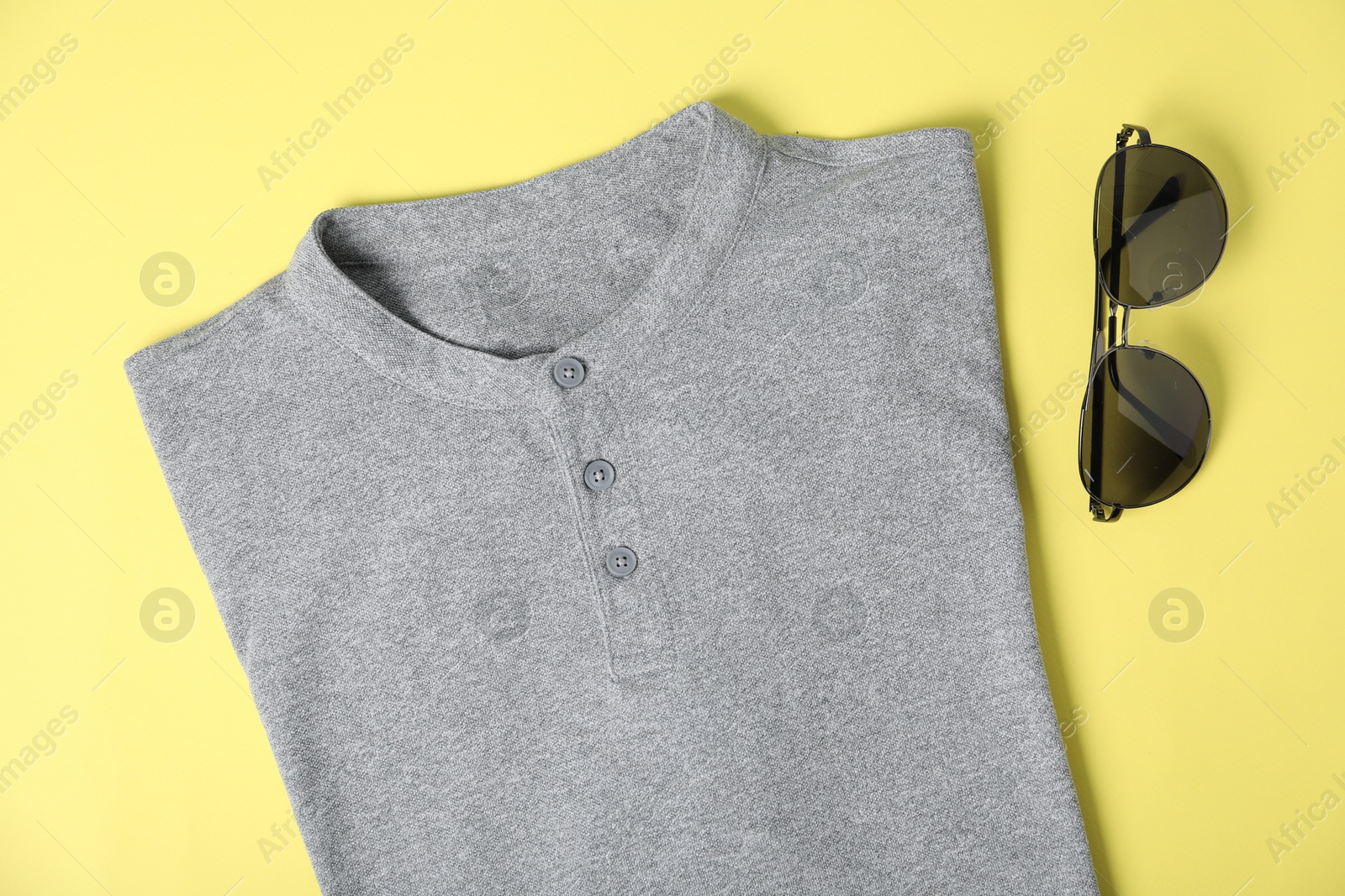 Photo of Grey t-shirt and sunglasses on yellow background, flat lay. Mockup for design